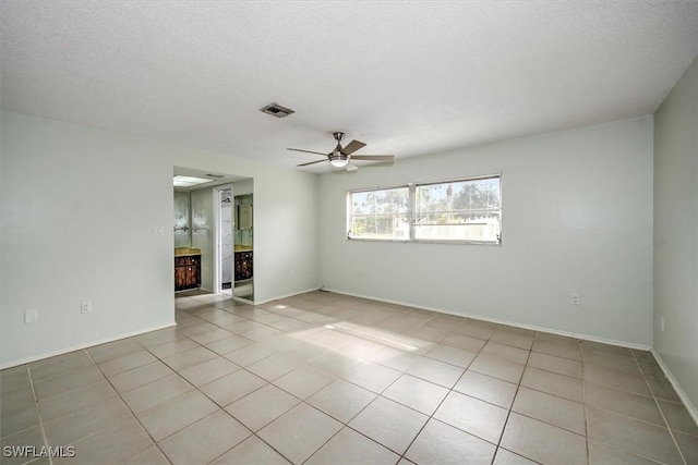 empty room with ceiling fan, light tile patterned floors, and a textured ceiling