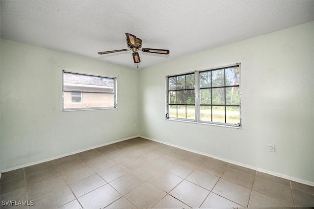 spare room with ceiling fan, light tile patterned floors, a wealth of natural light, and a textured ceiling