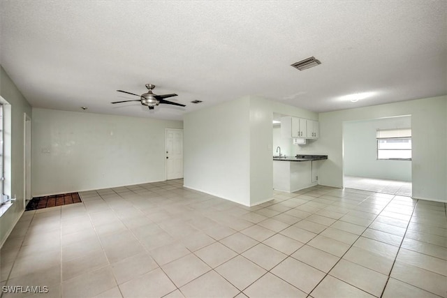 unfurnished living room with a textured ceiling, ceiling fan, light tile patterned floors, and sink