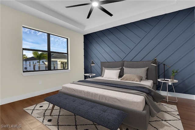 bedroom featuring an accent wall, wood finished floors, a ceiling fan, and baseboards