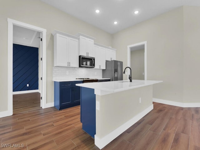 kitchen with appliances with stainless steel finishes, white cabinets, light countertops, and a center island with sink