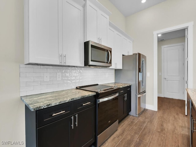 kitchen featuring light stone countertops, stainless steel appliances, white cabinetry, wood finished floors, and tasteful backsplash
