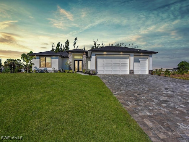 prairie-style house featuring decorative driveway, a front lawn, stucco siding, and stone siding