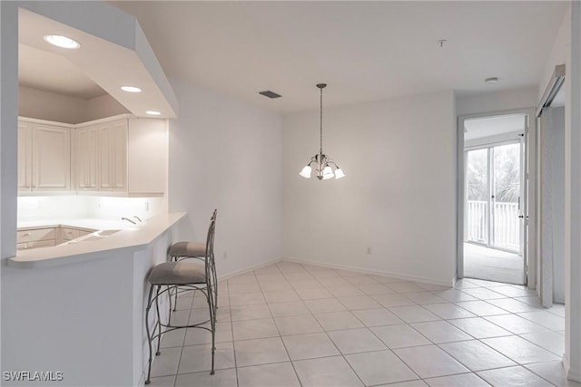 kitchen featuring light tile patterned floors, white cabinetry, a kitchen bar, a notable chandelier, and hanging light fixtures