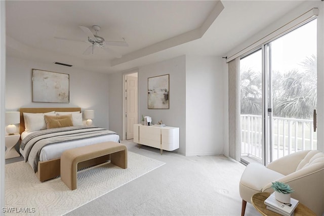 carpeted bedroom featuring ceiling fan, access to exterior, and a tray ceiling