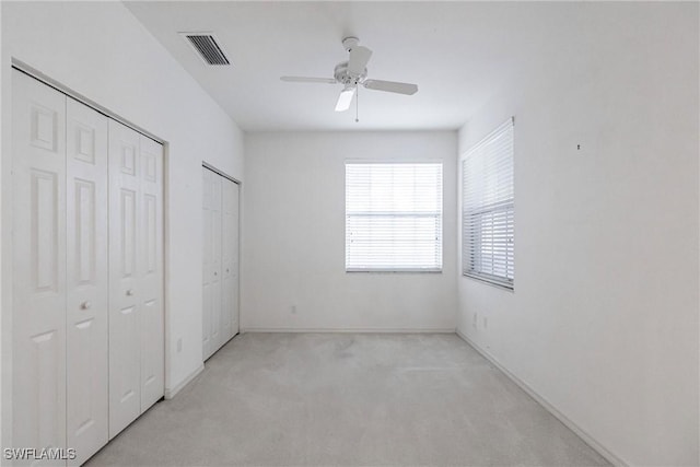 unfurnished bedroom featuring ceiling fan, multiple closets, and light carpet