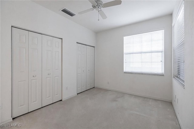 unfurnished bedroom with light carpet, ceiling fan, two closets, and multiple windows