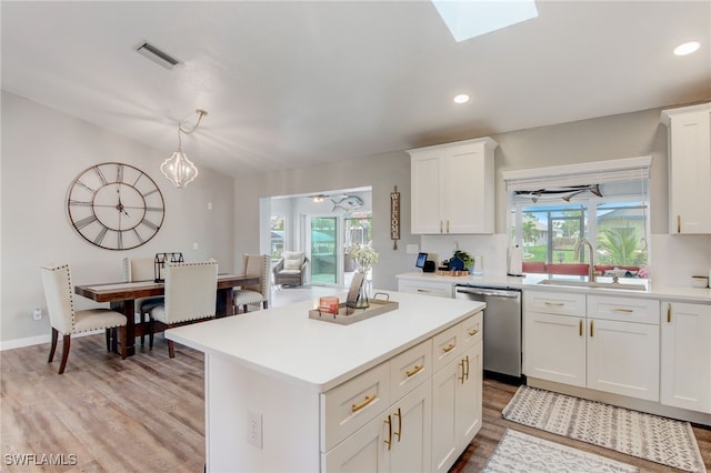 kitchen featuring a skylight, decorative light fixtures, dishwasher, white cabinets, and sink