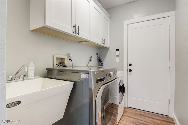 laundry area featuring light wood-type flooring, cabinets, washer and clothes dryer, and sink