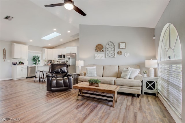 living room with light wood-type flooring, ceiling fan, and lofted ceiling with skylight