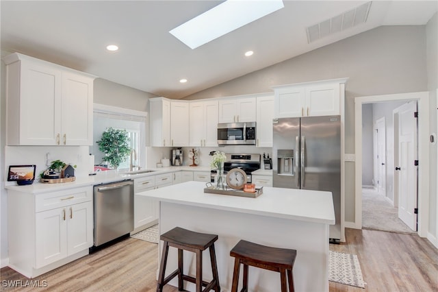 kitchen with vaulted ceiling with skylight, a center island, a breakfast bar, white cabinetry, and appliances with stainless steel finishes