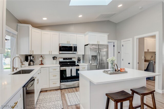 kitchen featuring stainless steel appliances, vaulted ceiling with skylight, washing machine and dryer, white cabinets, and sink