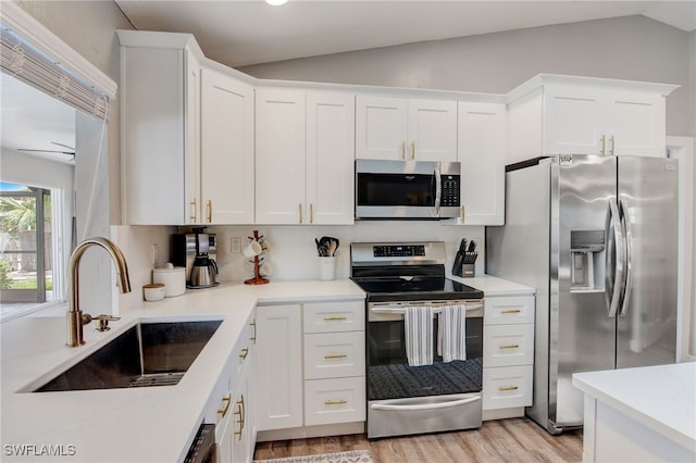 kitchen featuring lofted ceiling, light hardwood / wood-style floors, sink, white cabinetry, and appliances with stainless steel finishes