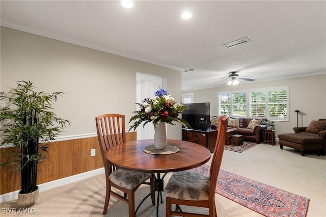 carpeted dining room with crown molding, ceiling fan, wooden walls, and a textured ceiling