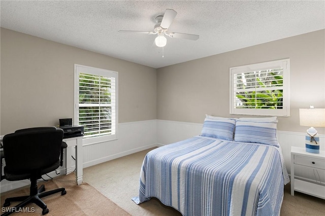 carpeted bedroom featuring ceiling fan, multiple windows, and a textured ceiling