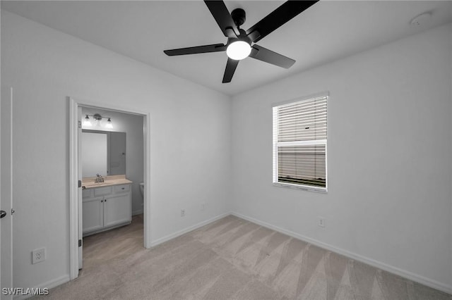 unfurnished bedroom with light carpet, ensuite bath, a sink, and baseboards