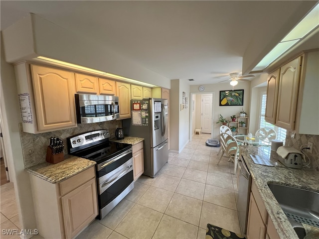 kitchen featuring appliances with stainless steel finishes, backsplash, ceiling fan, light stone counters, and light tile patterned floors