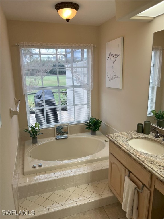 bathroom featuring a relaxing tiled tub, tile patterned flooring, vanity, and a healthy amount of sunlight