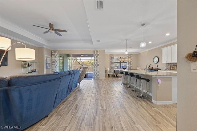 living room featuring ceiling fan, light wood-type flooring, a tray ceiling, and crown molding