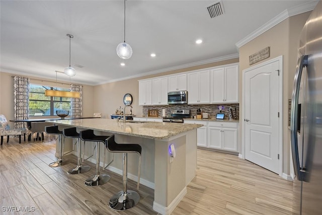 kitchen featuring white cabinetry, an island with sink, stainless steel appliances, hanging light fixtures, and sink