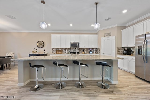 kitchen with pendant lighting, white cabinets, stainless steel appliances, and an island with sink