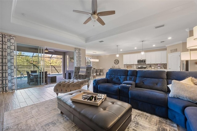 living room featuring ceiling fan, wood finished floors, visible vents, a tray ceiling, and crown molding