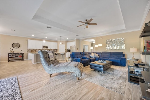 living room with ceiling fan, a tray ceiling, and ornamental molding