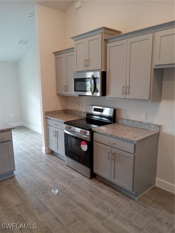 kitchen with light stone counters, appliances with stainless steel finishes, and gray cabinets