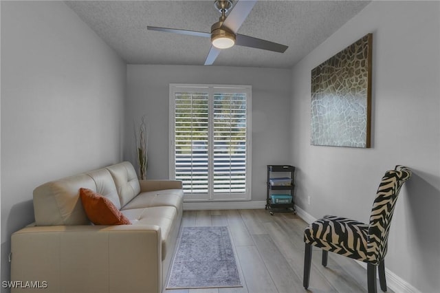 sitting room featuring ceiling fan, light wood-type flooring, and a textured ceiling