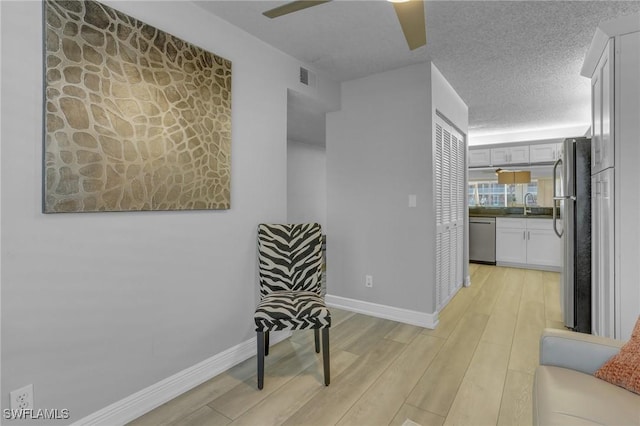 corridor with light hardwood / wood-style floors, sink, and a textured ceiling