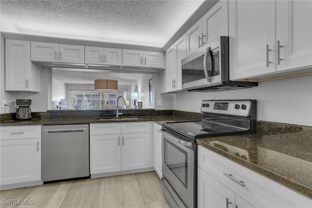 kitchen featuring dark stone counters, sink, stainless steel appliances, and white cabinetry