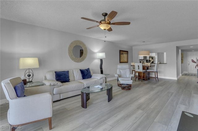 living room featuring ceiling fan, a textured ceiling, and light wood-type flooring