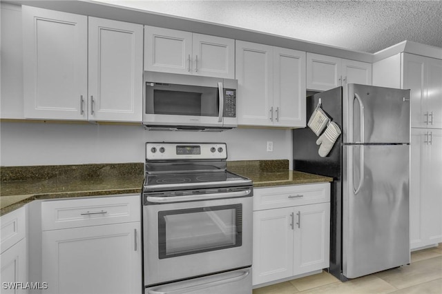 kitchen with appliances with stainless steel finishes, dark stone countertops, and white cabinetry