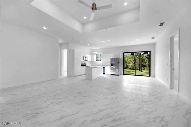 unfurnished living room with ceiling fan, a tray ceiling, and sink