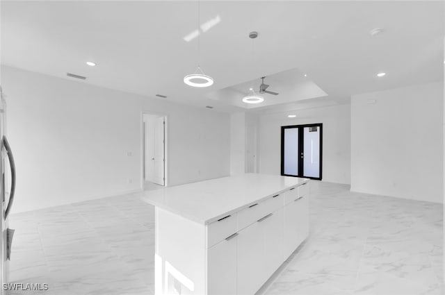 kitchen with white cabinetry, decorative light fixtures, a raised ceiling, a kitchen island, and ceiling fan