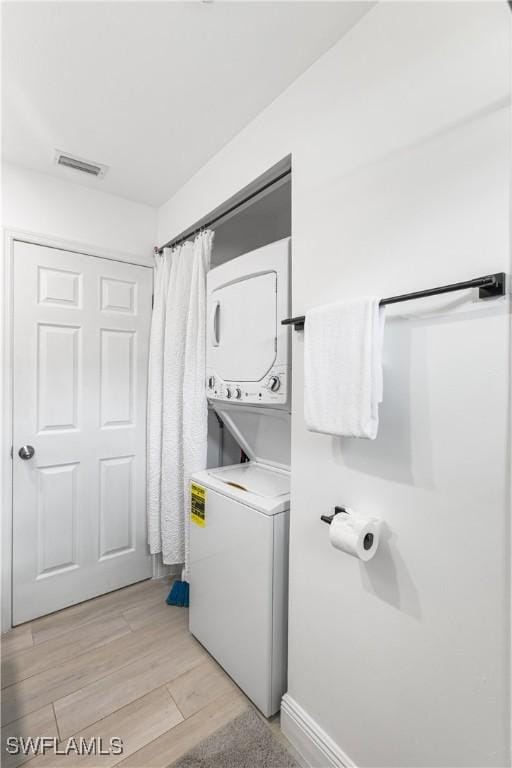 laundry room featuring stacked washer / dryer and light wood-type flooring