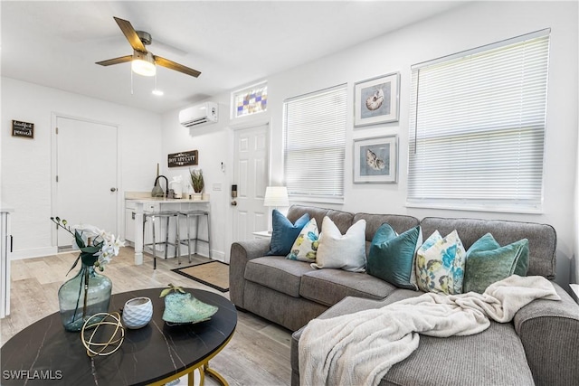 living room featuring ceiling fan, sink, a wall unit AC, and light hardwood / wood-style floors