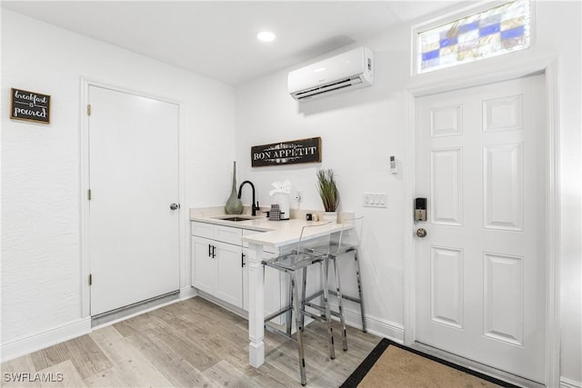 interior space featuring sink, white cabinets, light hardwood / wood-style flooring, and a wall unit AC