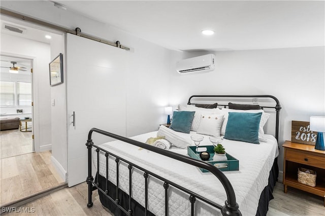 bedroom with a wall unit AC, a barn door, and light wood-type flooring