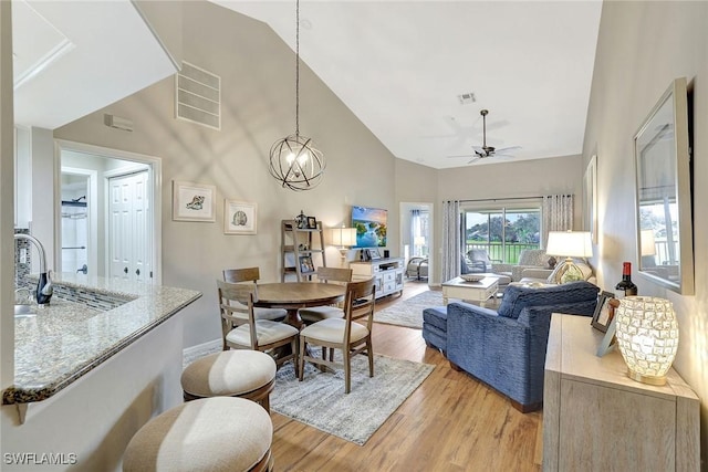 dining room featuring high vaulted ceiling, sink, ceiling fan with notable chandelier, and light wood-type flooring