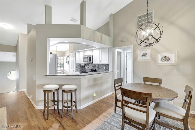 kitchen featuring white cabinets, stainless steel appliances, decorative backsplash, light hardwood / wood-style floors, and kitchen peninsula