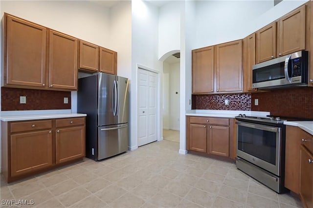 kitchen featuring backsplash, a towering ceiling, light tile patterned flooring, and stainless steel appliances