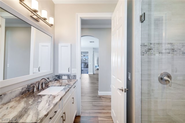 bathroom featuring a shower with shower door, hardwood / wood-style flooring, vanity, and ornamental molding