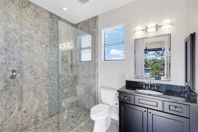 bathroom with toilet, a wealth of natural light, a tile shower, and vanity