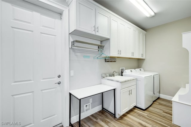 laundry area featuring light wood-type flooring, sink, separate washer and dryer, and cabinets