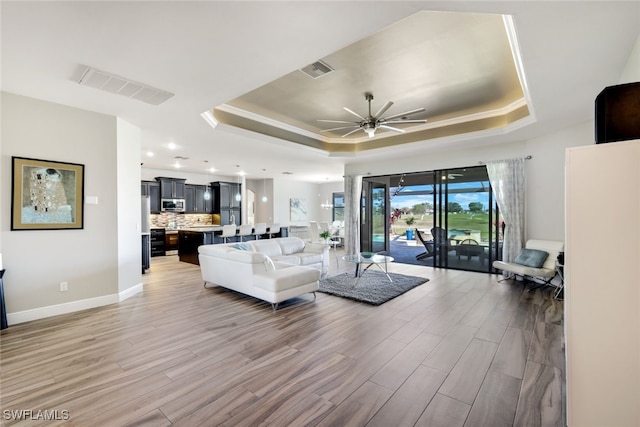 living room with ceiling fan, wood-type flooring, and a tray ceiling