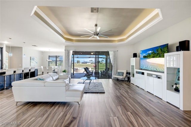 living room with ceiling fan, crown molding, hardwood / wood-style flooring, and a raised ceiling