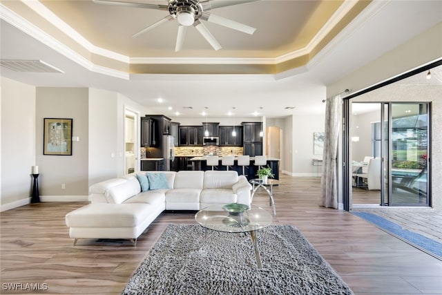 living room featuring ceiling fan, wood-type flooring, crown molding, and a tray ceiling