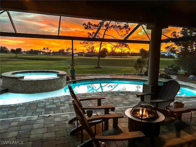 pool at dusk featuring a yard, a patio, a fire pit, and an in ground hot tub