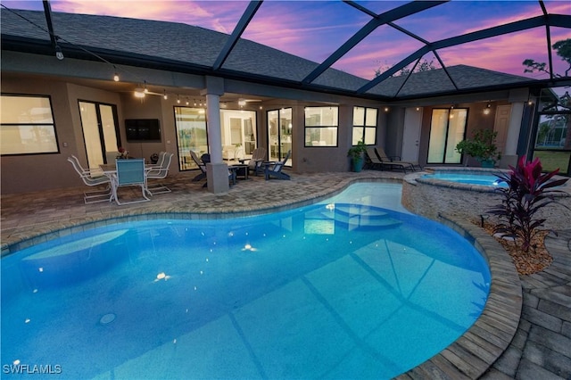 pool at dusk featuring an in ground hot tub, a patio area, and a lanai